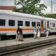 Group of adults walking beside a train at a platform in Bandung, Indonesia, outdoors during the day.